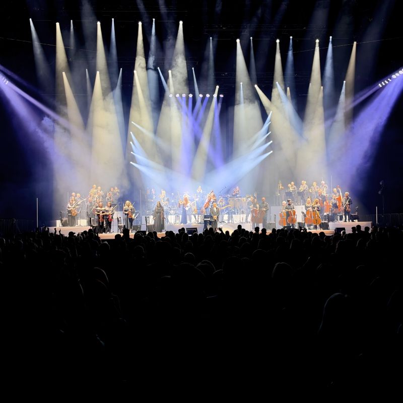 Orchestra performing beneath beams of light at the OVO Hydro